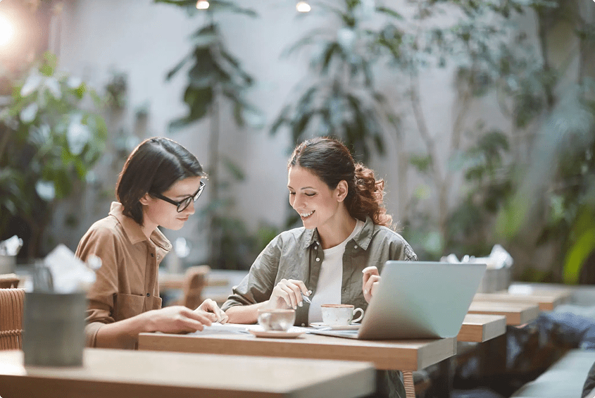 Two women wearing masks discussing at a table with a laptop.