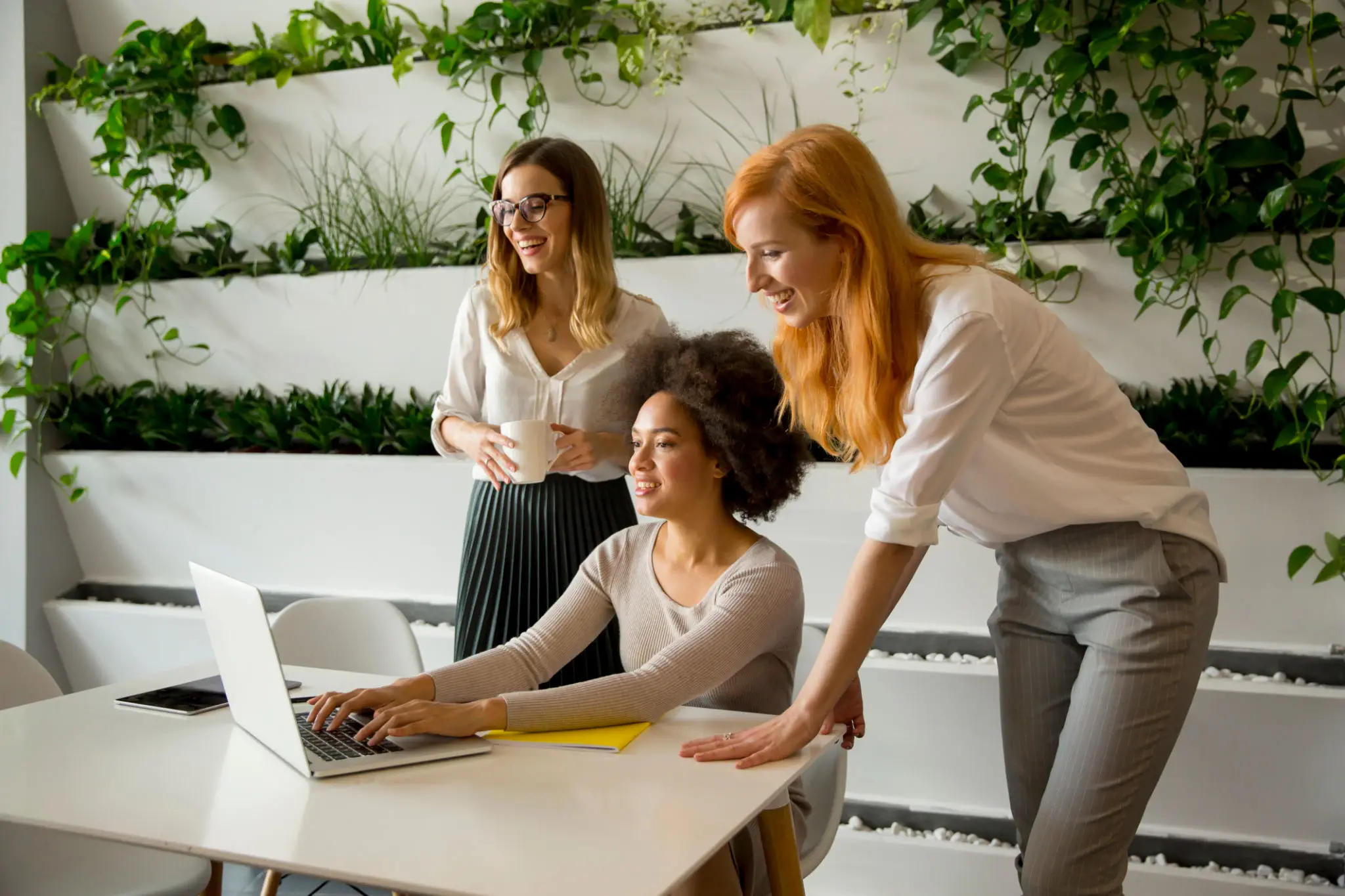 Three women collaborating on a project using a laptop in a bright office.